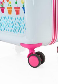 Maleta rígida con un acabado blanco brillante, decorada con coloridas macetas de flores, presenta detalles en rosa y ruedas giratorias para mayor movilidad.