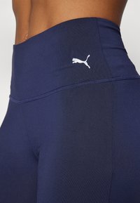 Mornarske tajice visokog struka od rastezljivog materijala, s bijelim Puma logotipom na pojasu i glatkom, teksturiranom površinom.