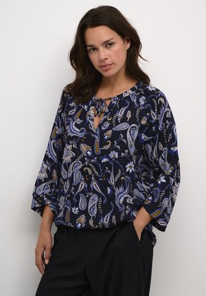 Marineblå bluse med paisley- og blomstermønstre. Har en bindebånd i halsen og trekvartlange ærmer. Lavet af et let, flodende stof.