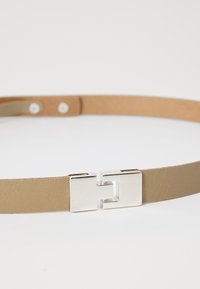 Ceinture en cuir tan avec une boucle rectangulaire en argent. La surface présente une texture lisse avec des détails de couture minimes.
