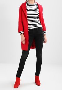 Rode jas, gestreept zwart-wit shirt met lange mouwen, zwarte spijkerbroek en rode laarzen met hoge hak. Gladde stof en nauwsluitende pasvorm.