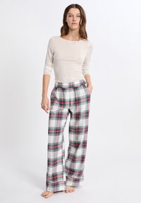 Witte langarmtop gecombineerd met geruite broek met rode, groene en blauwe patronen; zachte stof; elastische tailleband; losse pasvorm.