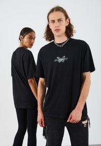 Black oversized t-shirts made of cotton with a butterfly graphic and the word "FLIGHT" printed in white, worn with distressed black jeans.