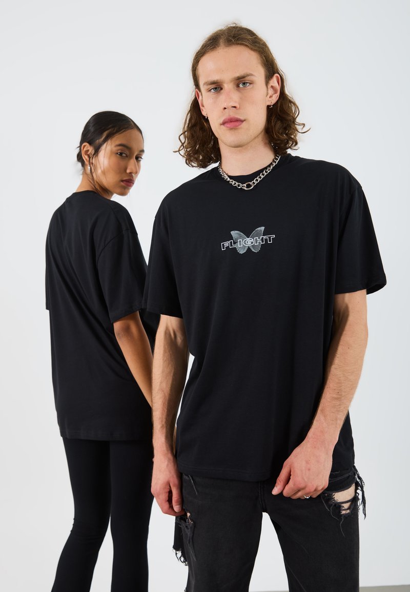 Black oversized t-shirts made of cotton with a butterfly graphic and the word "FLIGHT" printed in white, worn with distressed black jeans.