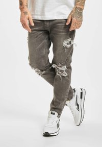 Gray distressed jeans with rips, paired with white sneakers featuring black accents. The jeans have a relaxed fit and a faded texture.