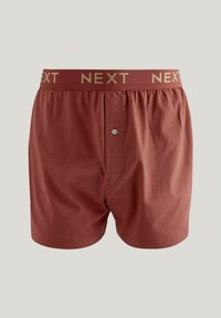 Rote Baumwoll-Boxershorts mit elastischem Bund, auf dem "NEXT" in goldenen Buchstaben steht, mit einer Knopföffnung und lockerer Passform.