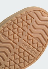 Adidas skosula i ljusbeige, med ett diamantmönster för grepp, texturerad yta och präglad logotyp nära hälen.