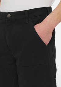 Sorte lærredsbukser med lige pasform, der har side lommer og en metalbranded knap. Struktureret stof med en let glans.
