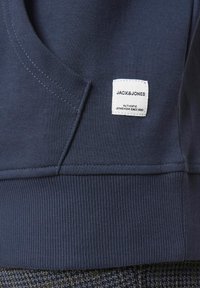 Sweatshirt marine avec un ourlet et des poignets côtelés. Présente une petite étiquette blanche avec un texte noir, des détails cousus et une texture douce.