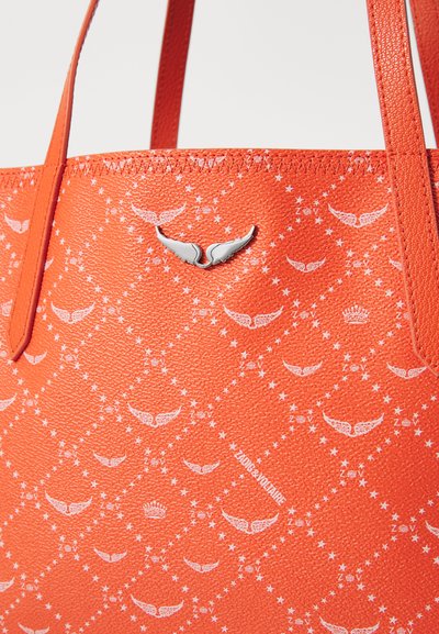 Orange Tragetasche aus strukturiertem Material mit weißen Flügelmotiven und Sternen, abgerundet mit einem Metall-Logo-Element. Doppelte Griffe.