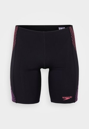 Shorts de bain noirs au design ajusté, présentant des rayures diagonales roses sur les côtés et un logo Speedo à l'avant. Fabriqués en matériau extensible.