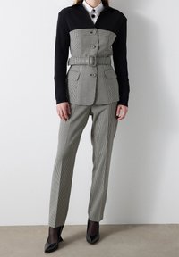 Traje a medida en blanco y negro de pata de gallo que presenta una chaqueta con cinturón y la parte superior en color contrastante, junto con pantalones a juego. Tejido de textura fina.