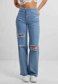 Svetlomodré vysoké džínsy s roztrhnutými kolenami. Materiál je denim s rovnými nohavicami. Nosené s bielymi teniskami.