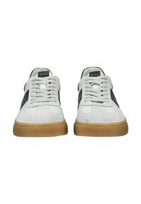 Pár bílých tenisek s černými bočními pruhy, bílými tkaničkami a podrážkami barvy gumy, zobrazených zepředu na bílém pozadí.