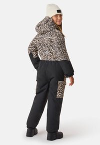 Isolierter Overall mit Leopardenmuster und schwarzem Unterteil, ausgestattet mit Kapuze, elastischen Bündchen und zwei Cargotaschen. Weiße Mütze ergänzt das Outfit.