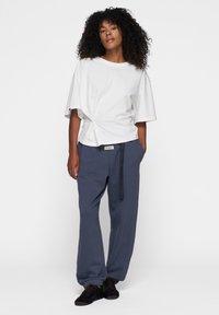 Witte katoenen t-shirt met een geknoopte voorkant, gecombineerd met donkerblauwe, ruimvallende sweatpants met een trekkoord en elastische boorden.