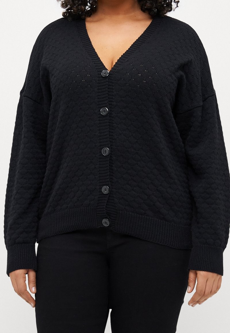 Cardigan nero con un motivo testurizzato, scollatura a V e grandi bottoni sulla parte anteriore. I polsini e l'orlo a costine aggiungono dettagli extra.