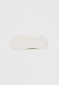 Talpă de pantof sport albă din cauciuc texturat, cu caneluri curbate și modele circulare pentru aderență. Logo-ul brandului este embossat în centru.