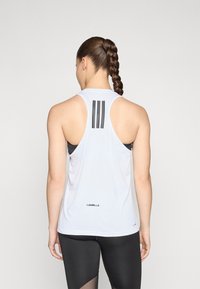 Top sport alb cu spate decupat, având trei dungi negre pe partea superioară a spatelui și un logo "LES MILLS" la tiv.