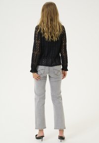 Blusa nera in pizzo con maniche lunghe, caratterizzata da un motivo testurizzato, abbinata a jeans svasati grigio chiaro e tacchi aperti neri.