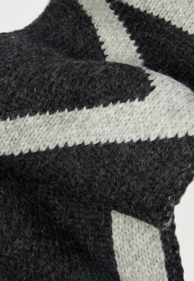 Sciarpa lavorata a maglia caratterizzata da una texture grigio scuro con un motivo a zigzag bianco. Materiale morbido con un aspetto cozy e spesso.