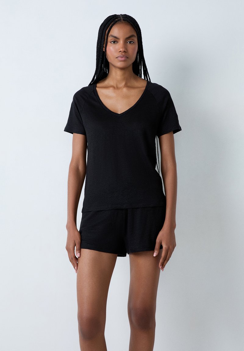 Zwarte kortemouw V-hals top met een gestructureerde stof, gecombineerd met bijpassende shorts. Beide stukken hebben een relaxed fit en een minimalistisch ontwerp.