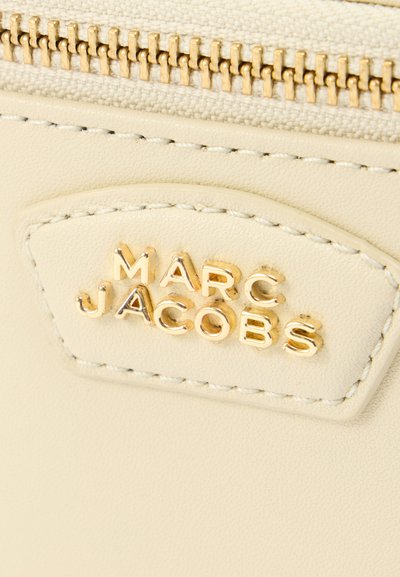 Δερμάτινο τσαντάκι σε κρεμ απόχρωση με φερμουάρ σε χρυσό τόνο. Διαθέτει ανάγλυφο λογότυπο «MARC JACOBS» πάνω από το φερμουάρ. Ομαλή υφή, μινιμαλιστικός σχεδιασμός.