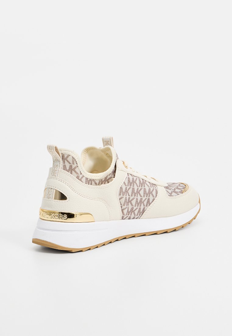 Beige Sportchuhe mit einem Obermaterial aus Mesh, das ein strukturiertes Logo-Muster aufweist, goldene Akzente und eine weiße Sohle mit einem hellbraunen Profil.