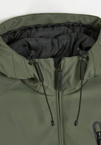 Oliwkowa kurtka z zamkiem błyskawicznym, czarną podszewką, regulowanymi sznurkami w kapturze oraz kontrastującymi akcentami przy zamku.