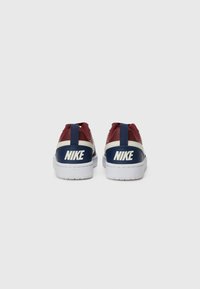 Sapatilhas vermelhas e azul-marinho com uma sola branca, apresentando um cabedal em couro e têxtil, detalhes contrastantes e uma marcação proeminente da Nike no calcanhar.