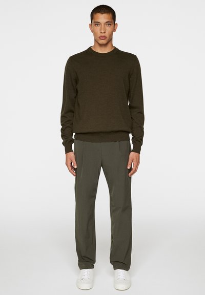Kaki-grön tröja med rund halsringning, i kombination med matchande smala byxor. Har ribbade manschetter och nederkant, bärs med vita sneakers.