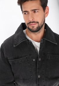 Giubbotto in denim nero con colletto classico, due tasche sul petto e chiusura con bottoni. Texture morbida con una finitura sbiadita e cuciture a contrasto.