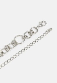 Bracciale in metallo argento a catena con grandi cerchi pieni e una catena più piccola, rifinito con un gancio a moschettone e un accento a forma di perla rotonda.