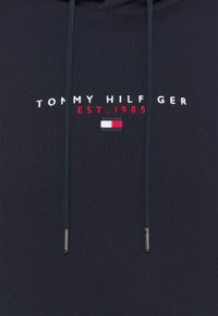 Sudadera azul marino con un logo bordado que dice "TOMMY HILFIGER EST. 1985" con una barra de acento tricolor en rojo, blanco y azul.