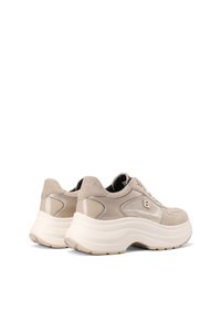 Sneaker in suede beige con suola bianca spessa, dettagli lucidi e sovrapposizioni testurizzate. Presenta lacci tondi e dettaglio del logo sul lato.