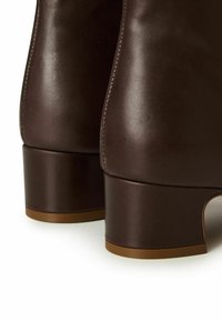 Stivali alla caviglia in pelle marrone con tacco a blocco arrotondato e texture liscia, con dettagli di cucitura discreti lungo le cuciture.