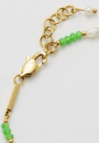 Bracciale in oro con perline verdi sfaccettate e perle bianche, dotato di chiusura a moschettone e un'etichetta incisa con la scritta "ESPRIT."