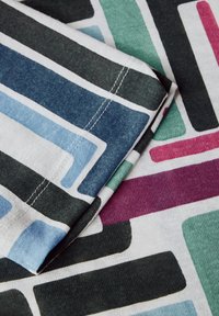 Tissu en coton avec de grands motifs rectangulaires en bleu, vert, noir et bordeaux sur un fond blanc, avec des détails de couture visibles.