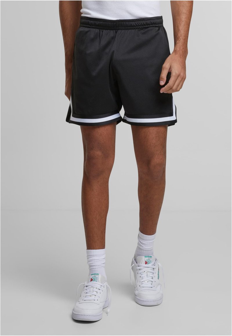 Shorts de sport noirs avec des rayures blanches sur les côtés, taille élastique et tissu texturé. Portés avec des baskets blanches et des chaussettes de longueur mi-mollet.