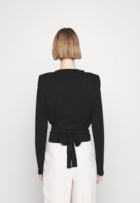Schwarzes Langarmoberteil mit einem gebundenen Rückendetail, gefertigt aus einem weichen Material, mit Rundhalsausschnitt und enganliegender Passform.