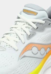 Białe buty biegowe z szarymi akcentami, z pomarańczowym logo i teksturowaną cholewką, z detalicznymi sznurowadłami oraz żywą żółto-pomarańczową podeszwą.