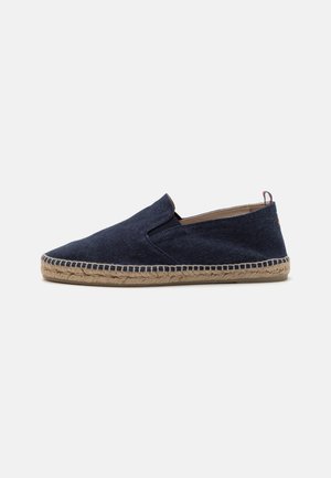 Sötétkék vászon espadrille kerek orral, jutas kötél talppal és slip-on kialakítással. Hangyás varrás és egy kis hátsó hurkos rész jellemzi.