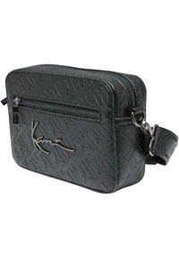 Svart faux läder crossbody-väska med präglat geometriskt mönster, blixtlåsfack och silverfärgad hårdvara. Justerbar rem ingår.