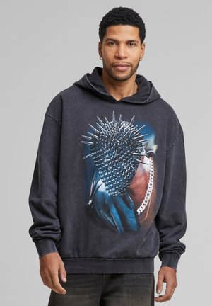 Sort bomulds hoodie med et grafisk design af et pigget objekt, med en afslappet pasform og lange ærmer. Kraven er hætte.