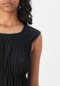 Black, sleeveless dress with a textured, pleated design and a gathered neckline. Features a relaxed fit and soft fabric texture.