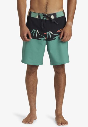 Herren Boardshorts in Türkis mit einem schwarzen Bund. Sie verfügen über einen tropischen Druck in dunklen Farben. Hergestellt aus schnelltrocknendem Material und mit einem Kordelzugverschluss.