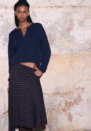 Cardigan tricoté bleu marine avec motifs torsadés et fermeture à boutons, associé à une jupe longueur genou aux rayures marron et bleu marine.
