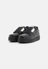 Sneaker in pelle nera con punta perforata, suola in gomma nera spessa e accenti di branding bianchi sulla linguetta e sul lato.