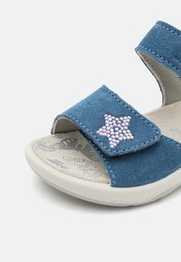 Blå ankelremssandal med stjernesformet rhinestone-accent, justerbar rem og en polstret, mønstret såle med sommerfugler.