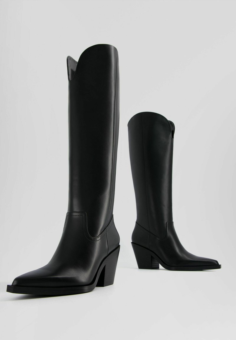 Bottes en cuir noir, montantes jusqu'au genou, avec un bout pointu, un talon carré et un design froncé. Présente une couture minimale et une texture lisse.